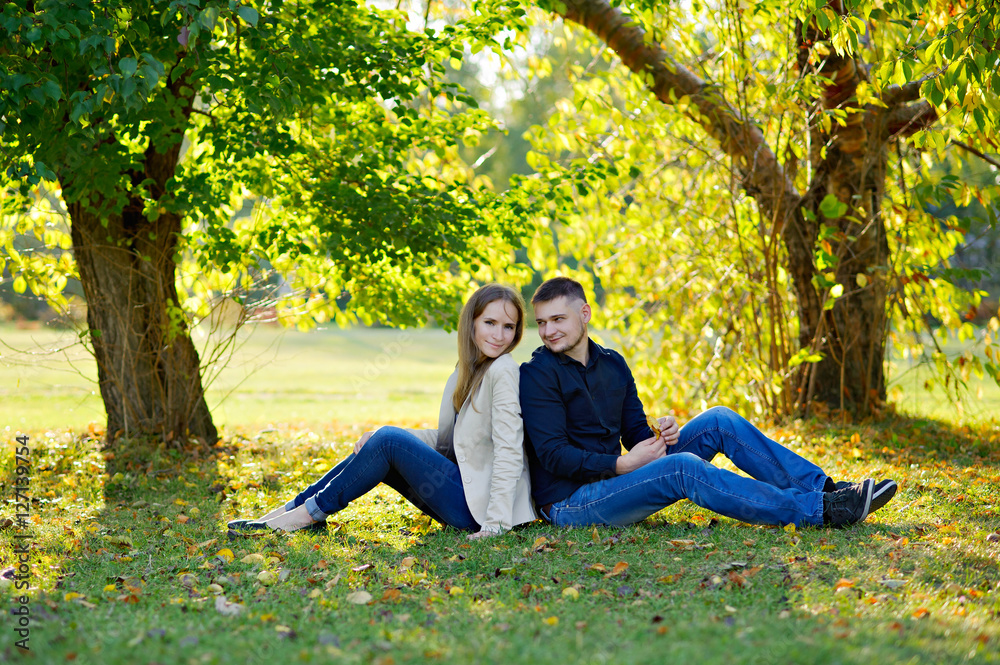 Man and woman sitting on the Sunny meadow under a spreading tree, full growth, fall. Man and woman sitting on the Sunny meadow under a spreading tree, full growth, fall.