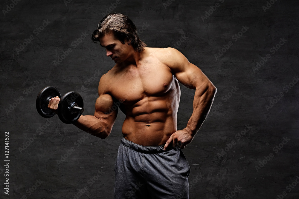 Shirtless muscular male holds dumbbell.