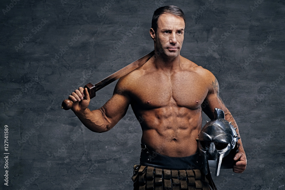 Middle age, muscular male holds silver gladiator helmet and an i Middle age, muscular male holds silver gladiator helmet and an i