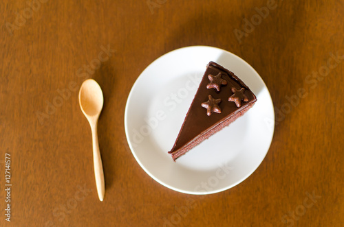 Piece of chocolate cake on white dish with wooden spoon ready to eating