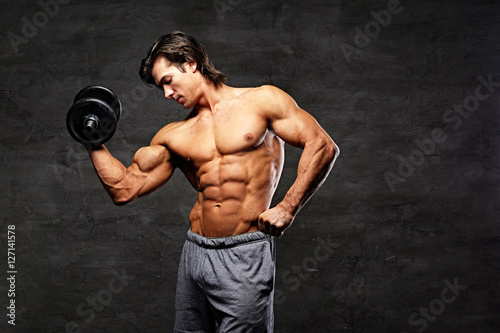 Shirtless muscular male holds dumbbell.