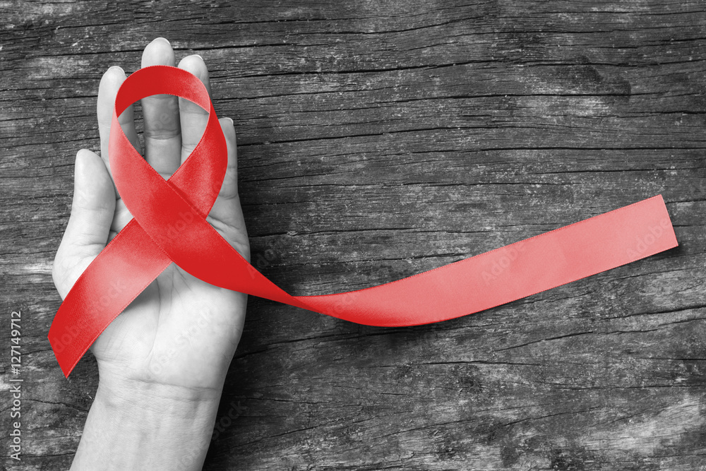 Red ribbon awareness on human hand with aged wood background with clipping path: World aids day: Symbolic concept for raising awareness campaign on people with HIV concept - obrazy, fototapety, plakaty 