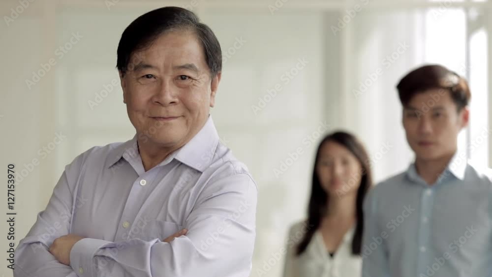 MS Senior business man folding arms with young colleagues behind him / Singapore MS Senior business man folding arms with young colleagues behind him / Singapore