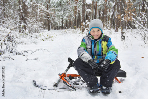 In winter, the snow-covered forest boy sitting on a sledge.