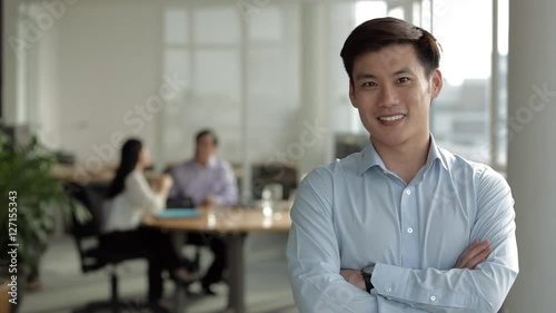 MS Businessman standing with arms folded in front of two colleagues, smiling / Singapore