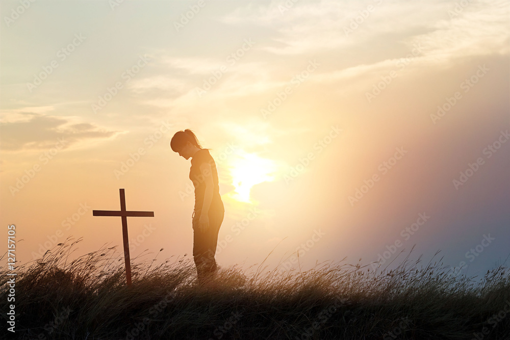 Woman respecting at the cross on the field of sunset background