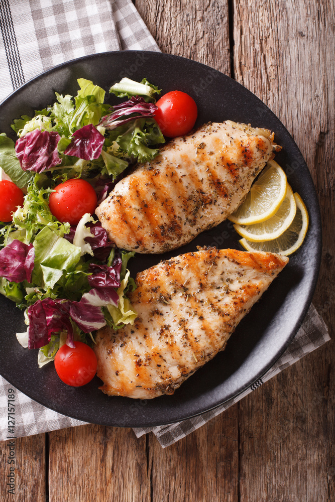 Grilled chicken breast with salad of chicory, tomatoes and lettuce close-up. Vertical top view Grilled chicken breast with salad of chicory, tomatoes and lettuce close-up. Vertical top view