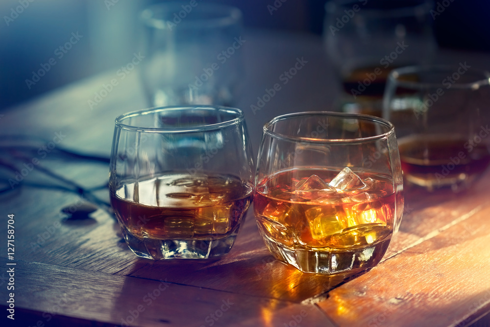Whiskey bourbon in a glass with ice on wooden table colorful background - obrazy, fototapety, plakaty 