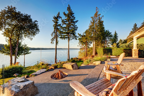 Back yard of waterfront house with adirondack chairs and fire pit photo