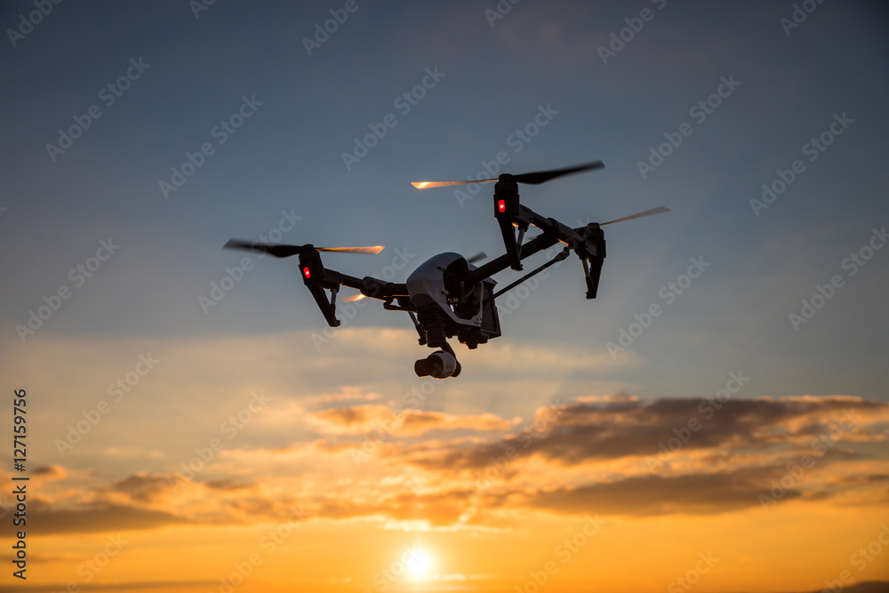 White drone with digital camera flying in sky over field on sunset White drone with digital camera flying in sky over field on sunset