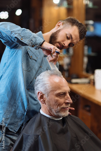 Handsome hairdresser making haircut to senior man