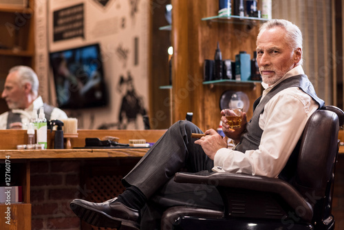 Elegant senior man with whiskey glass and cigar at barbershop