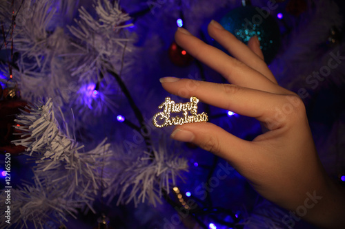 merry christmas sign in woman hands near christmas tree, closeup