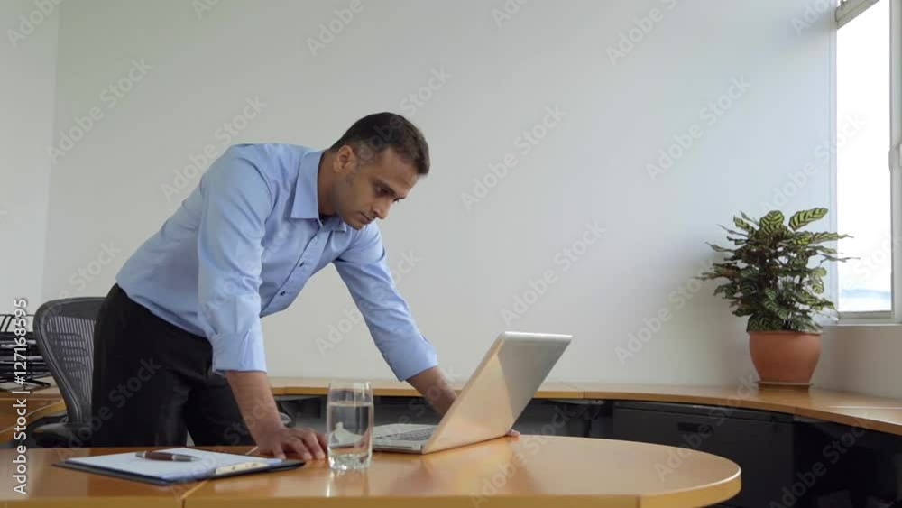 SELECTIVE FOCUS Businessman leans on desk looking at his laptop / Singapore