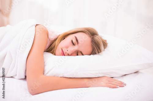 view of tired beautiful young woman with long hair sleeping on bed in bedroom