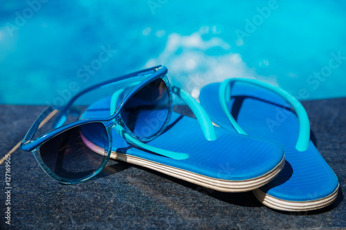Blue slippers and sunglasses on border of a swimming pool - holiday tropical concept