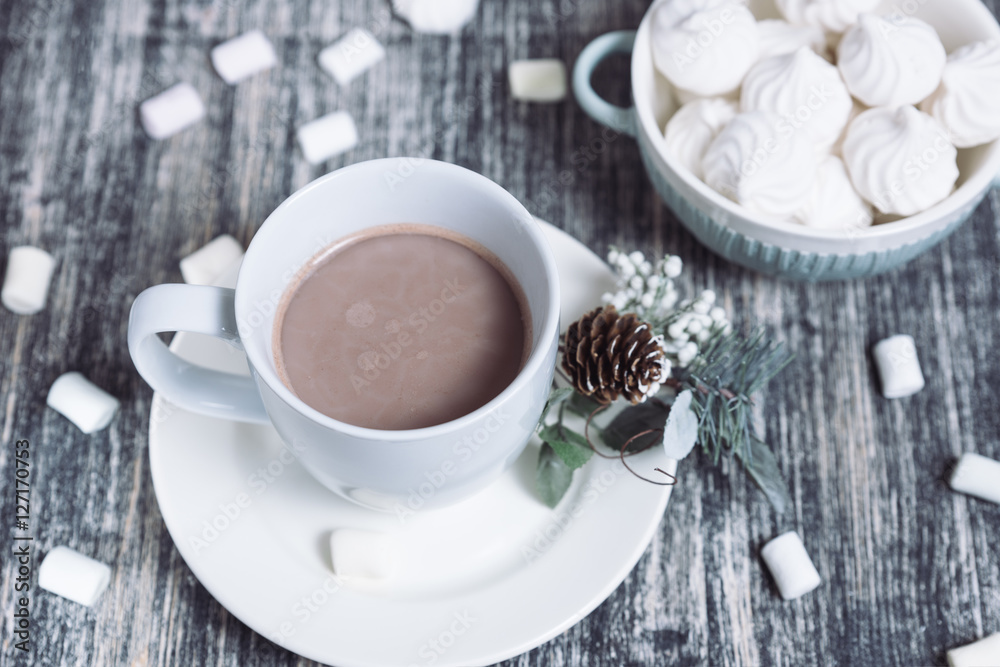 Hot chocolate with marshmallows. Drink in a white ceramic cup with zephyr on wooden table. Decorative pine branch with the cone on plate, saucer Hot chocolate with marshmallows. Drink in a white ceramic cup with zephyr on wooden table. Decorative pine branch with the cone on plate, saucer