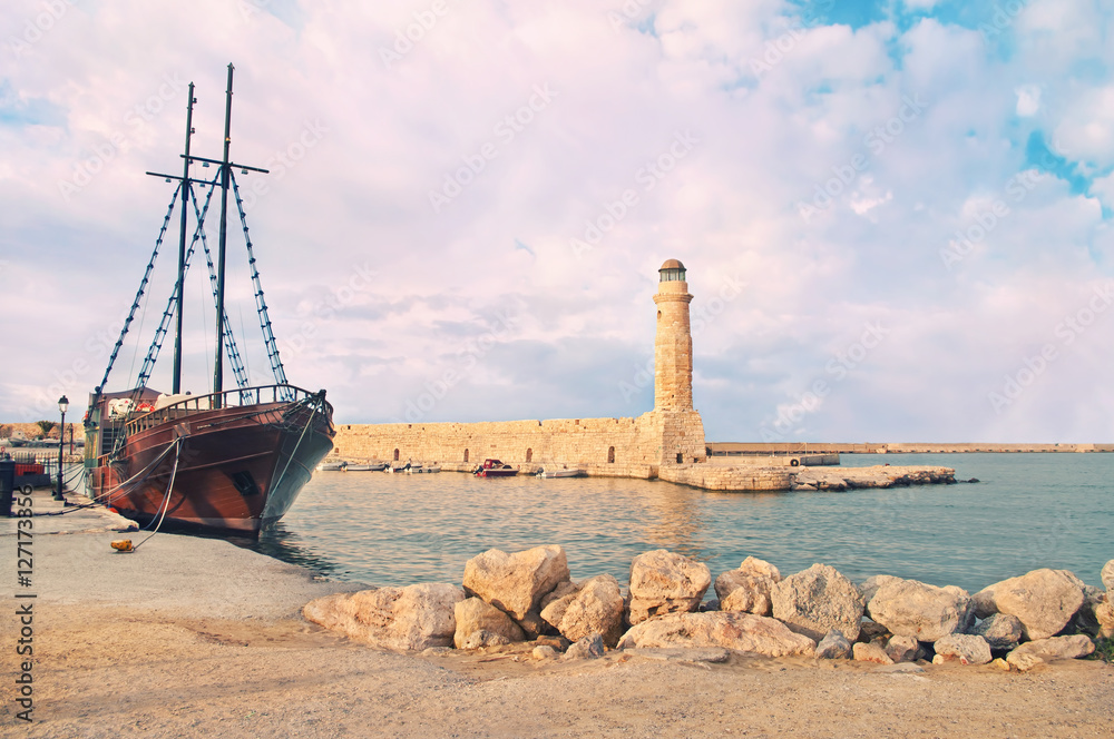 stone lighthouse and beautiful old ship at sunset