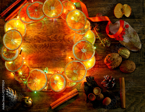 Christmas hand made craft template evening light background. Make traditional New Year`s door wreath components: tree cones, dried oranges, cinnamon, ribbon and colorful garland lights. Copyspace.