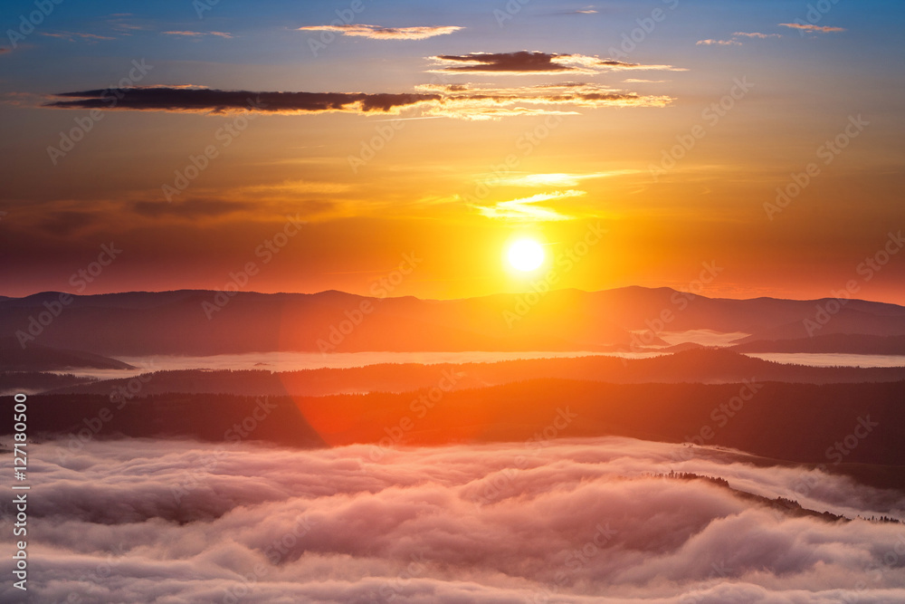 Summer weather phenomenon. Seasonal landscape with morning fog in valley. Clouds drenched valley below the level of the mountains. Sunrise over creeping clouds.