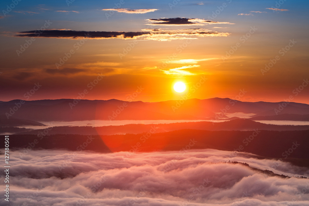 Summer weather phenomenon. Seasonal landscape with morning fog in valley. Clouds drenched valley below the level of the mountains. Sunrise over creeping clouds.