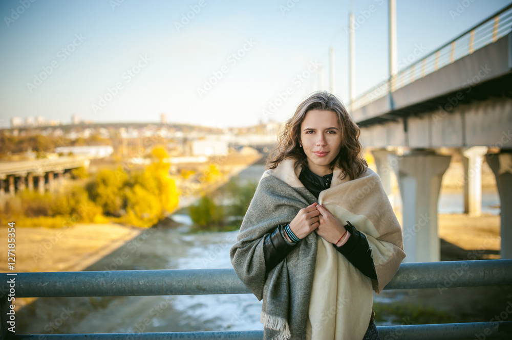 portrait of a beautiful young woman with long thin hair, a leather jacket, blue jeans. warm autumn sunny day on the stairs of the bridge.