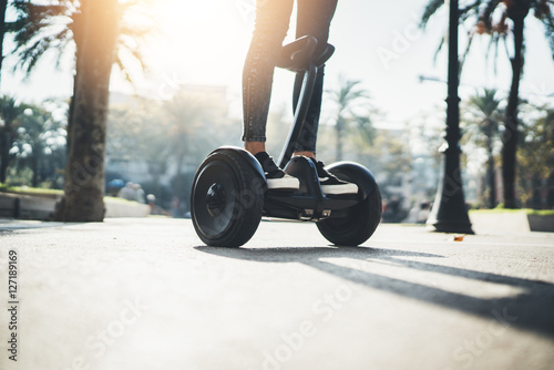 Young hipster girl driving on hoverboard at sunny park, active woman balancing on modern electric segway, alternative transport concept, ecology and environment concept, flare light photo