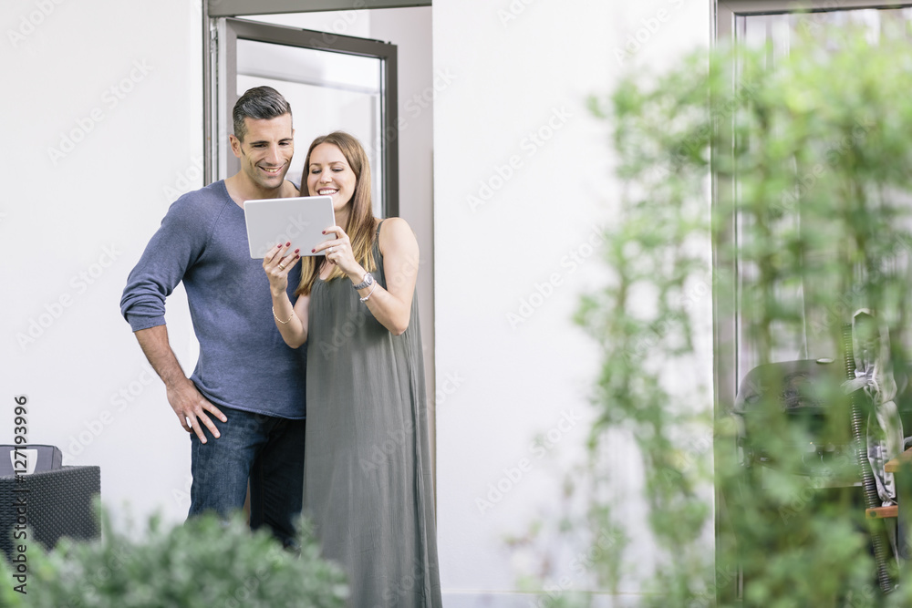 Smiling couple at terrace door sharing tablet Smiling couple at terrace door sharing tablet