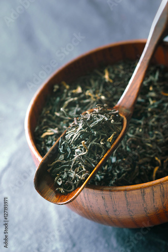 Картината върху платно Tea leaves on the wooden bowl  with spoon on the   stone background vertical