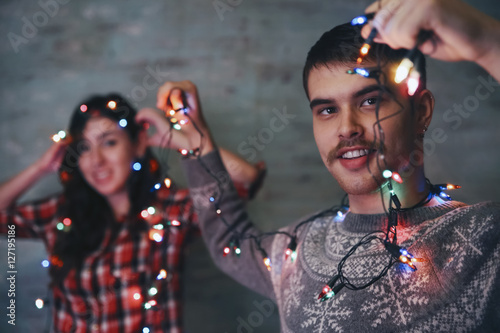 Young man holding fairy lights while his girlfriend watching in the background photo