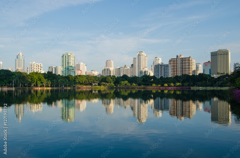 the skyline of metropolis building with the green park and blue sky background , the city park reflection from water in lake.