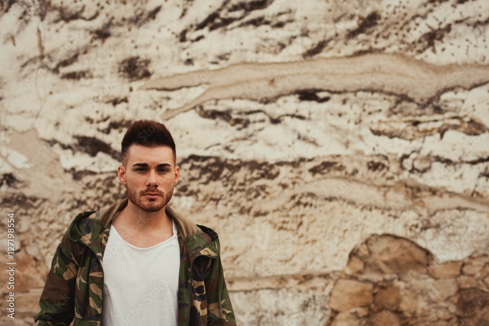Attractive guy with jacket military stylish on a wall of mud Attractive guy with jacket military stylish on a wall of mud