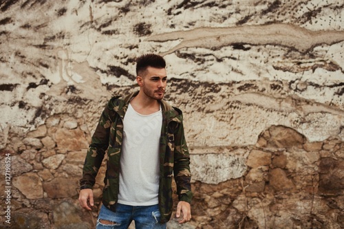 Attractive guy with jacket military stylish on a wall of mud