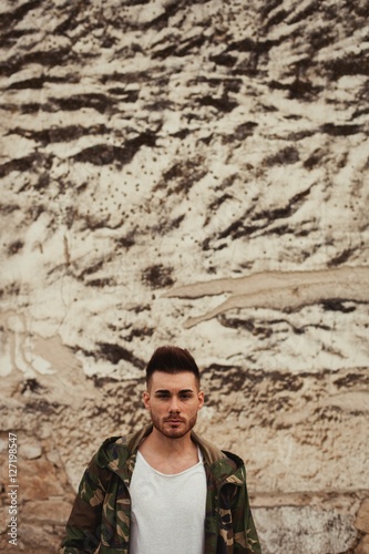 Attractive guy with jacket military stylish on a wall of mud