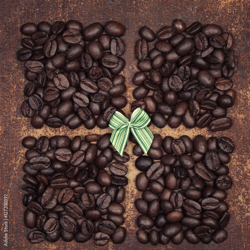Small green bow on dark roasted coffee beans divided into quarters on a faux leather material background