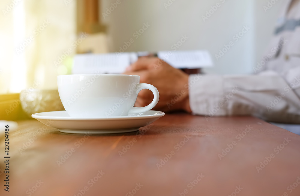 Man reading a book with white coffee cup front place.