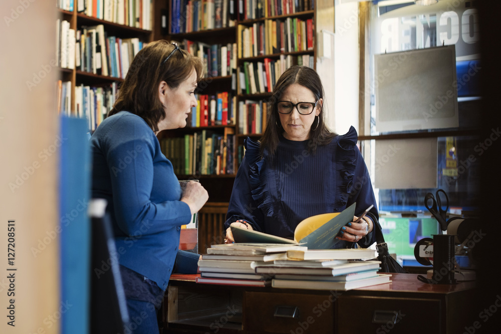 Female customer discussing with librarian standing in bookstore Female customer discussing with librarian standing in bookstore