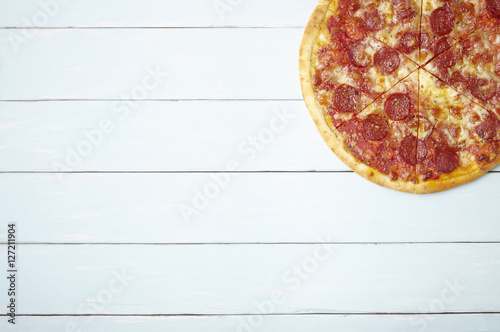 A whole, cooked and sliced peperoni pizza on a painted wooden table top background with empty space at side
