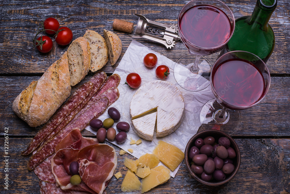 Red wine in a glass and a set of products - cheese, sausage, salami, olives, tomatoes, hot peppers, bread on a wooden board, background Red wine in a glass and a set of products - cheese, sausage, salami, olives, tomatoes, hot peppers, bread on a wooden board, background