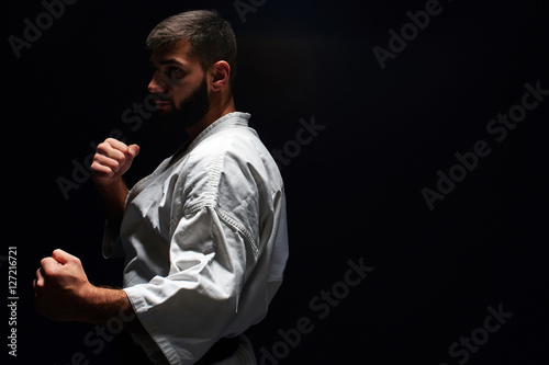 Karate man in a kimono in fighting stance on a black background