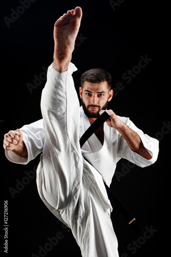 Karate man in a kimono hits foot on a black background