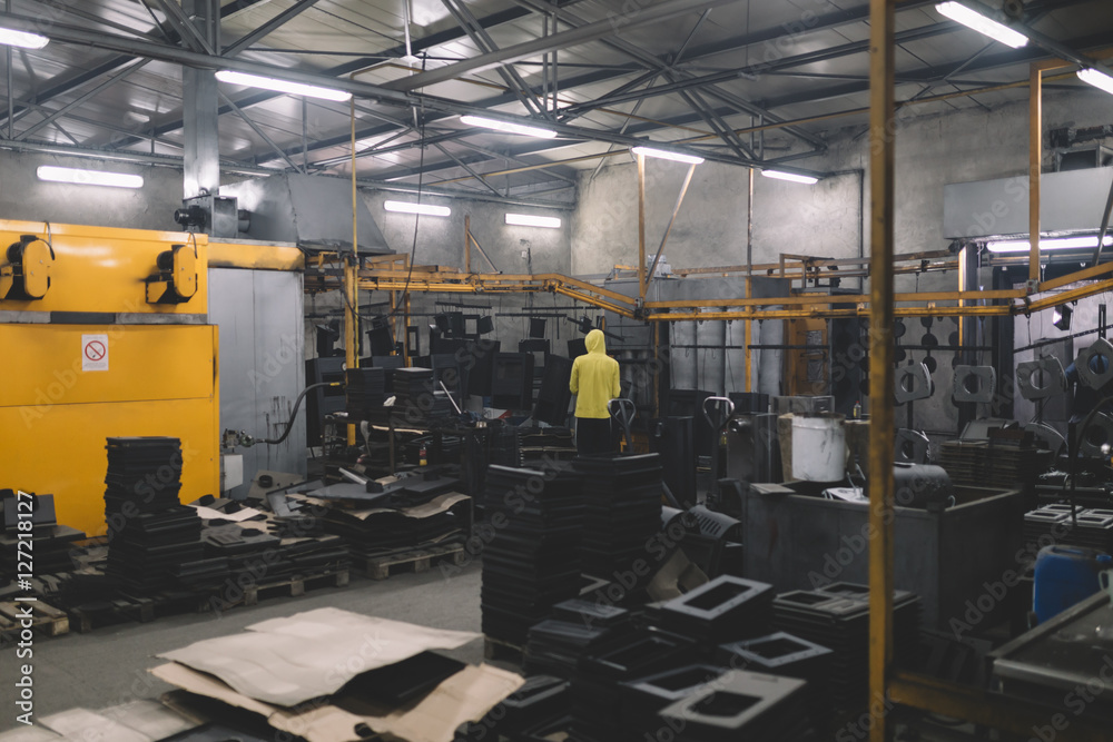 Metallurgy industry. Factory for production of heavy pellet stoves and boilers. Manual worker painter on his job. Extremely dark conditions and visible noise. Focus on foreground.