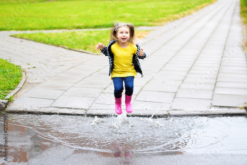 Happy cute little girl jumping in puddle after rain in summer