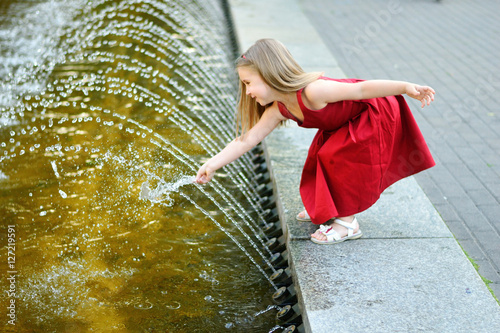 Cute little girl playing with a city fountain on hot and sunny summer day