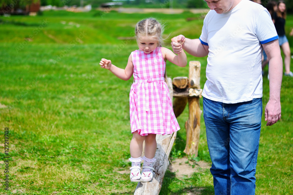 Adorable little girl with father holding her hand walking on wood on sunny summer day Adorable little girl with father holding her hand walking on wood on sunny summer day