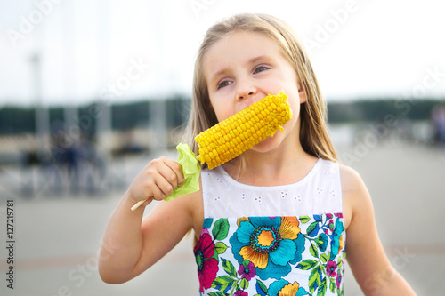 Adorable funny girl eating corn on the cob on sunny summer day