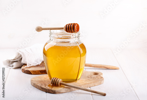 Glass jar of honey and wooden dipper on white