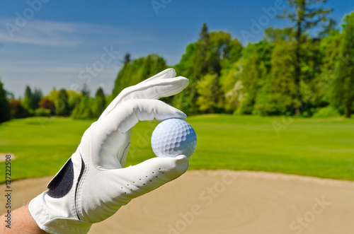 hand showing golf ball over sand bunker at beautiful golf course with blue sky