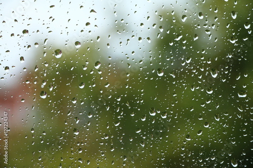 Rain drops on window with building and green tree in background 