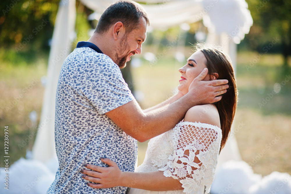 Happy pregnant couple stay hugging and loving near decor arch at Happy pregnant couple stay hugging and loving near decor arch at